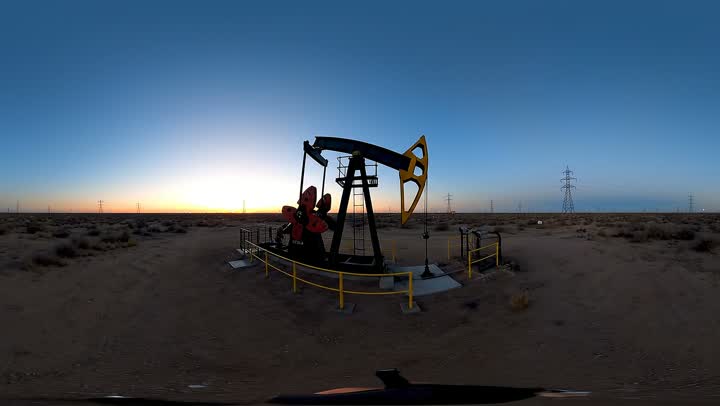 A pumpjack turning against a wide Texas sky at dusk, transmission towers on the horizon behind it