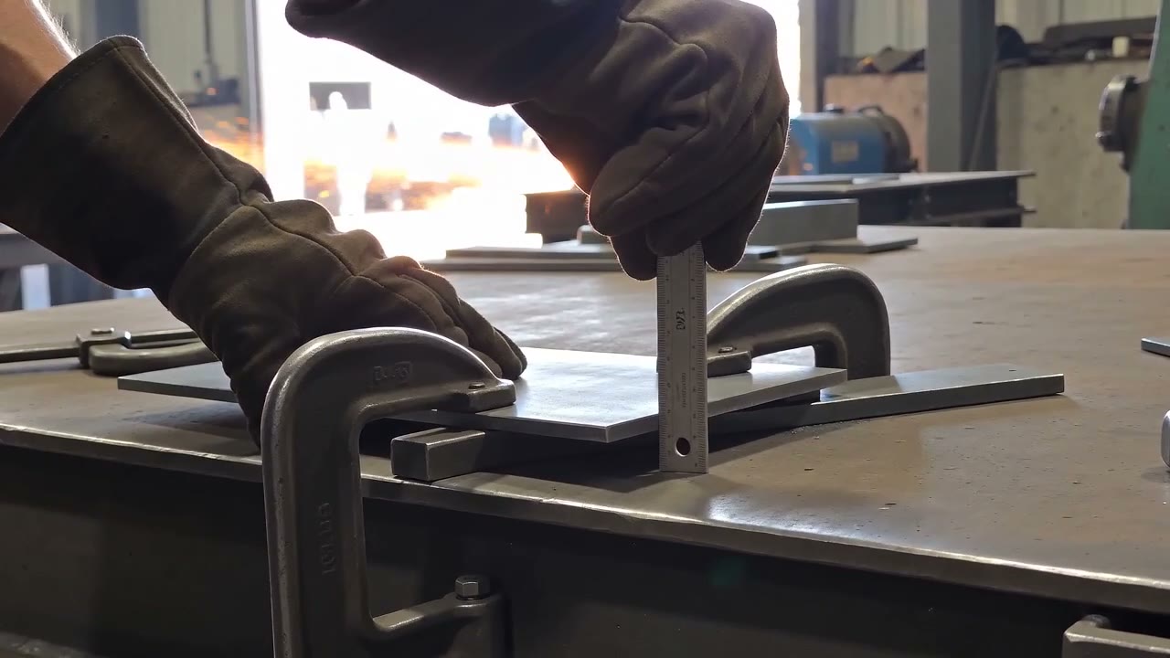 Gloved hands squaring steel plate on a fabrication bench